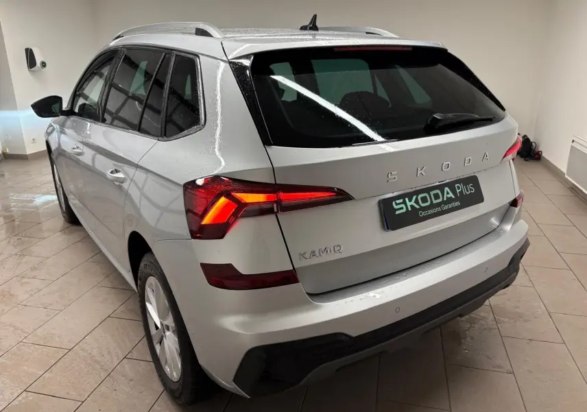 Vue 3/4 arrière gauche du Skoda Kamiq gris argent 2025 avec feux arrière allumés et caméra de recul visible.