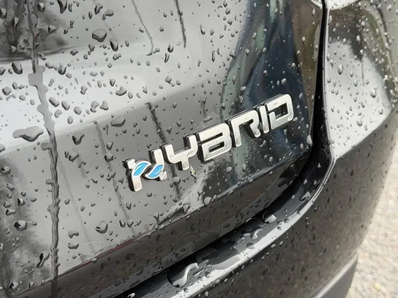 Gros plan sur l’inscription "Hybrid" argentée avec détail bleu sur la malle arrière noire mouillée d’une Fiat 600.