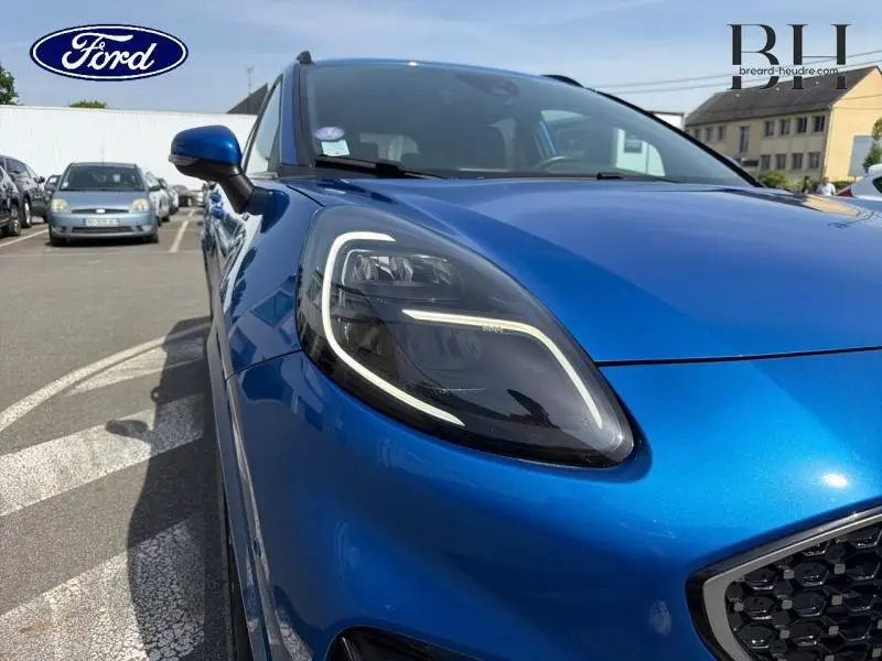 Gros plan sur le phare avant gauche du Ford Puma bleu Fashion Island métallisé avec calandre et rétroviseur assortis.