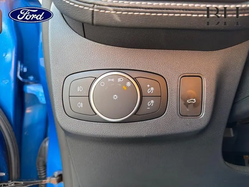 Gros plan sur le bouton de commande des phares et l'ouverture du hayon, intérieur noir du Ford Puma bleu côté conducteur.