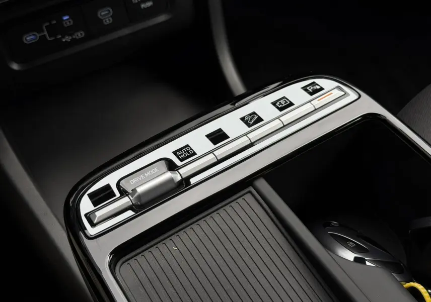 Gros plan sur la console centrale du Hyundai Tucson 2026, boutons argentés et surface noire brillante avec rangement coulissant.