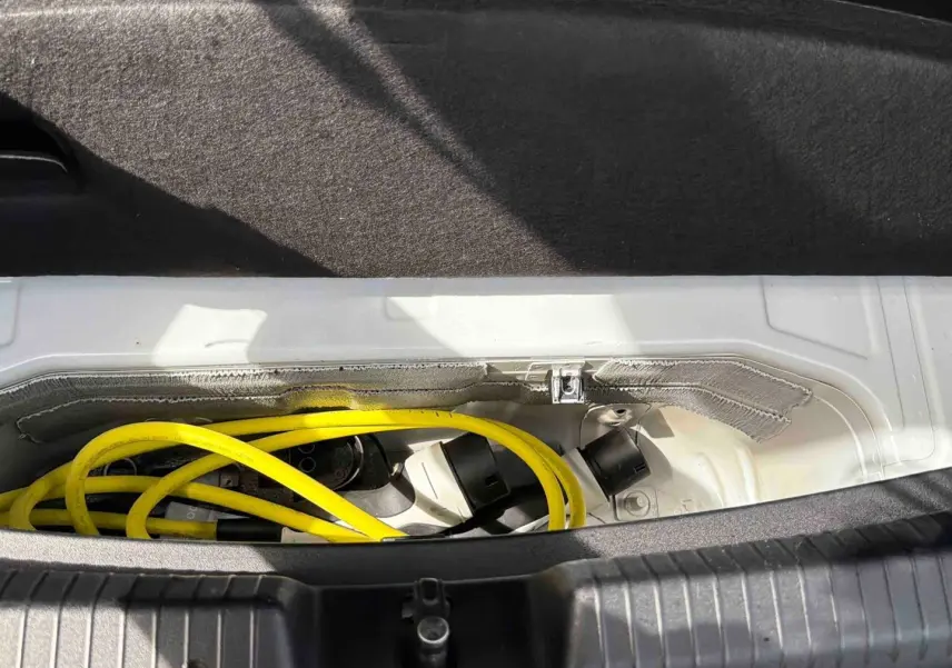 Coffre ouvert montrant le câble de recharge jaune du CUPRA Born e-boost blanc, vue rapprochée intérieure arrière.