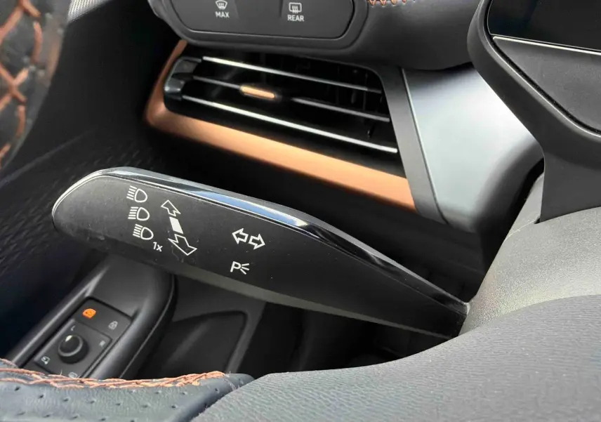 Gros plan sur la manette de clignotant noire à gauche du volant, avec coutures marron visibles sur le volant du CUPRA Born blanc.