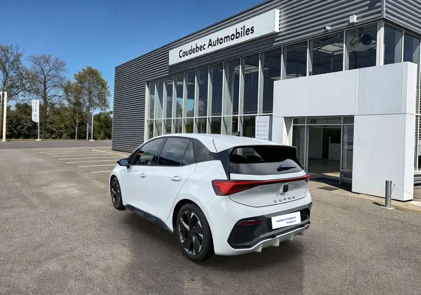 Vue 3/4 arrière d'une CUPRA Born blanche avec jantes Typhoon Black, feux LED et vitres arrière surteintées.