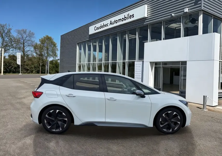 Profil côté gauche de la CUPRA Born électrique blanche 2024 avec jantes alliage noires devant un showroom.