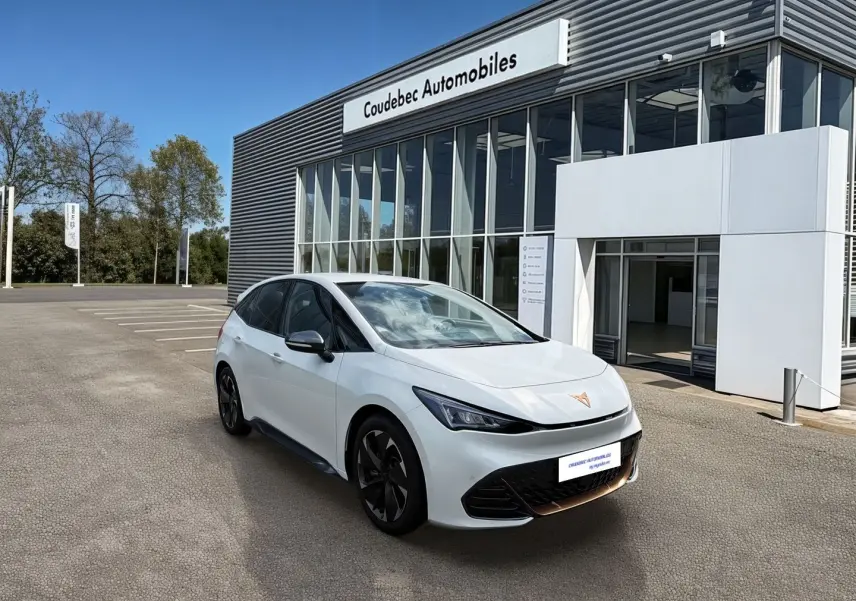 Vue 3/4 avant droite d'une CUPRA Born blanche avec jantes alliage noires devant un bâtiment de concession automobile.