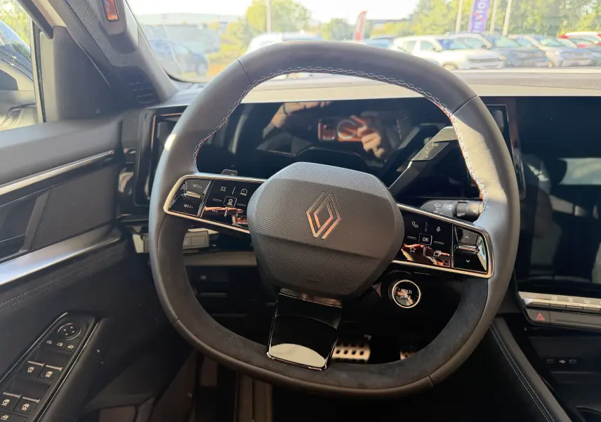 Vue rapprochée du volant chauffant du Renault Austral E-Tech 200 Esprit Alpine avec surpiqûres tricolores et tableau de bord numérique.