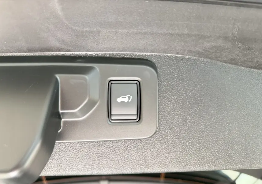 Bouton d'ouverture électrique du hayon sur la garniture intérieure du coffre d'un Renault Austral blanc nacré toit noir.