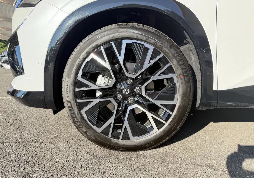 Gros plan sur la jante avant droite noire et argentée du Renault Austral blanc nacré avec passage de roue noir.