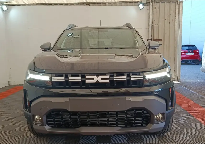 Vue de face du Dacia Duster Journey Hybrid 155 noir avec calandre distinctive et feux LED allumés.