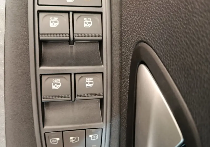 Gros plan sur les commandes des vitres électriques et réglages des rétroviseurs côté conducteur du Dacia Duster noir 2026.