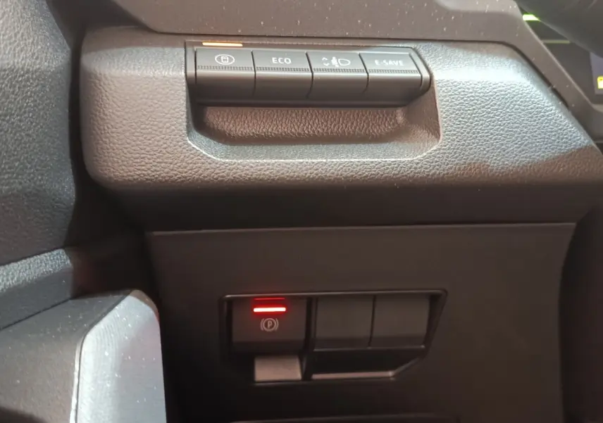 Gros plan sur les commandes noires du tableau de bord du Dacia Duster Journey Hybrid 155, avec bouton frein à main électrique allumé.