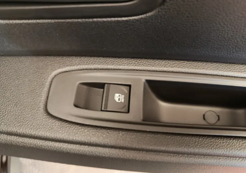Gros plan sur le bouton de commande de la vitre électrique côté porte intérieure d’un Dacia Duster noir.
