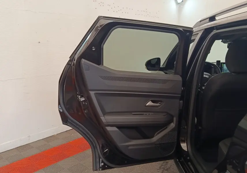 Vue intérieure de la porte arrière droite ouverte d'un Dacia Duster Journey Hybrid 155 noir, montrant les détails de la garniture.