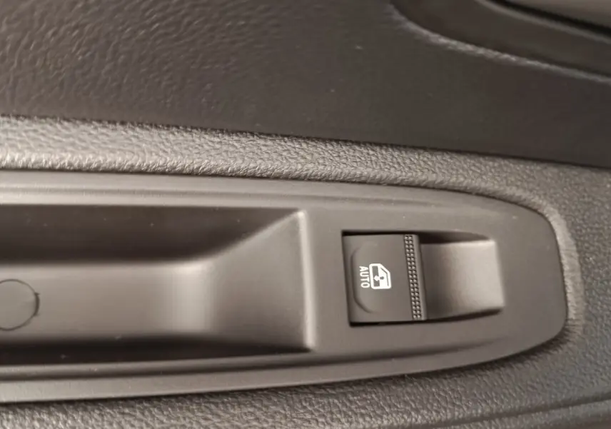 Gros plan sur le bouton de commande de la vitre électrique automatique côté conducteur du Dacia Duster noir 2026.