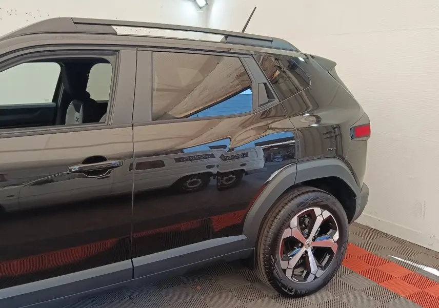 Vue latérale droite du Dacia Duster Journey Hybrid 155 noir, mettant en valeur la roue arrière et les rails de toit noirs.