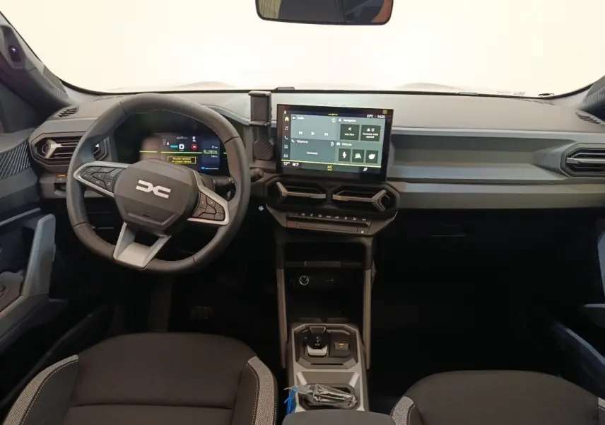 Vue intérieure avant du tableau de bord du Dacia Duster Journey Hybrid 155 avec écran tactile central et volant multifonctions.
