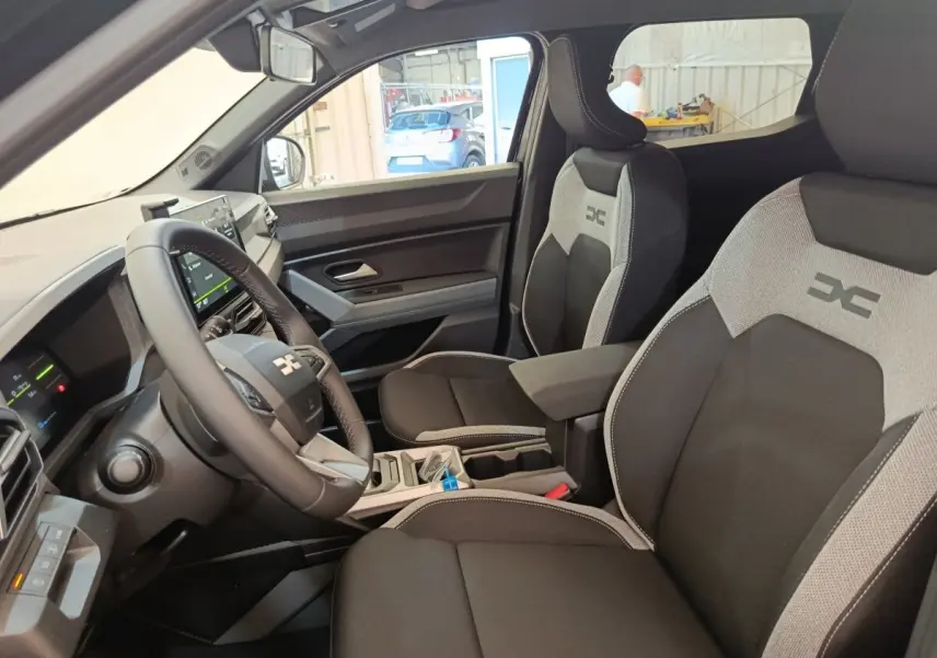 Vue intérieure côté conducteur du Dacia Duster Journey Hybrid 155 avec sièges noirs et gris et volant multifonctions.