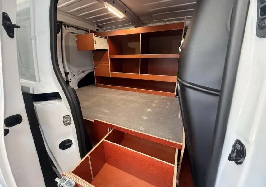 Vue intérieure côté gauche du Citroën Berlingo blanc 2019, montrant un aménagement bois avec étagères et tiroir ouvert.