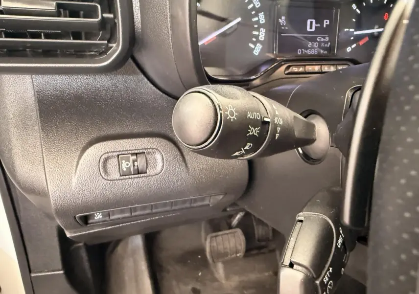 Gros plan sur la commande des phares et le tableau de bord noir du Citroën Berlingo blanc, vue côté conducteur.