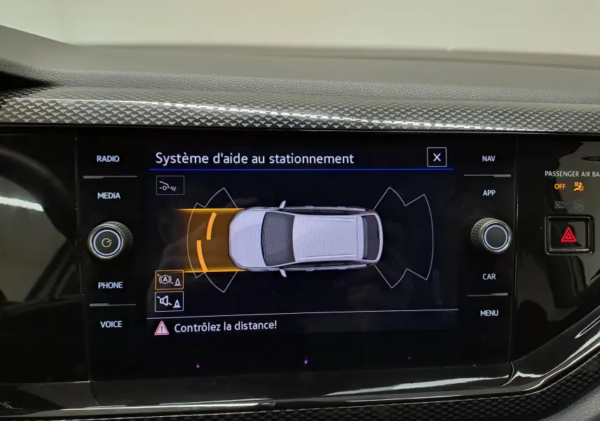 Écran tactile du système d'aide au stationnement du Volkswagen Taigo blanc, affichant une vue aérienne du véhicule et alertes de proximité.