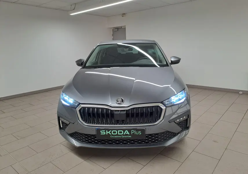 Vue frontale d'une Skoda Scala 2025 gris graphite avec phares allumés et calandre marquée SKODA Plus.