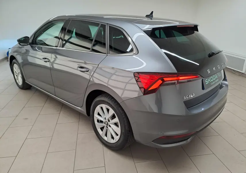 Vue 3/4 arrière droite d'une Skoda Scala gris graphite métallisé avec feux allumés et caméra de recul visible.
