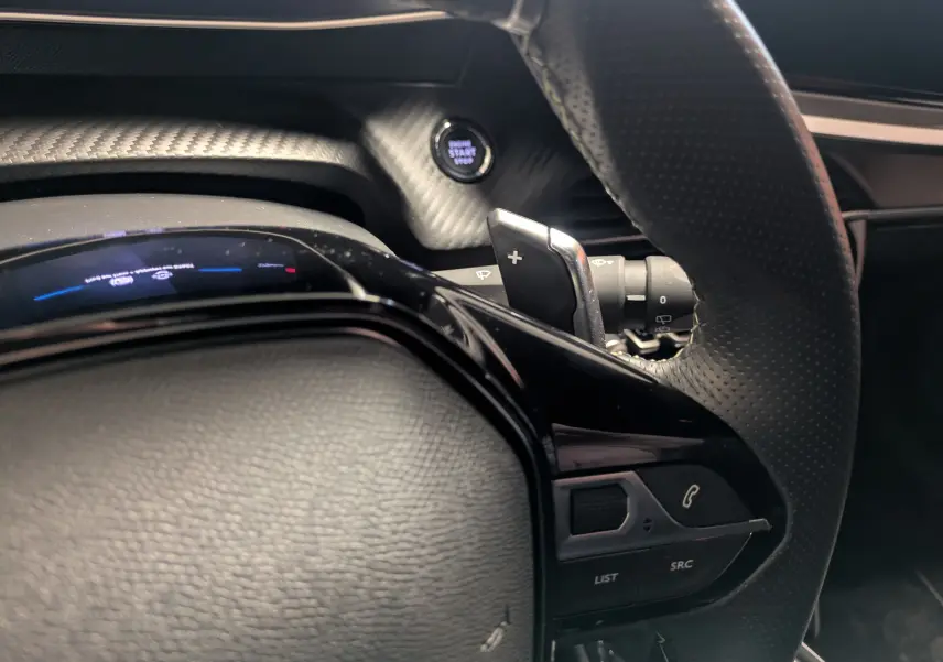 Gros plan sur le volant perforé et les commandes multifonctions du Peugeot 2008 Hybrid 145 e-DCS6 GT, intérieur noir.