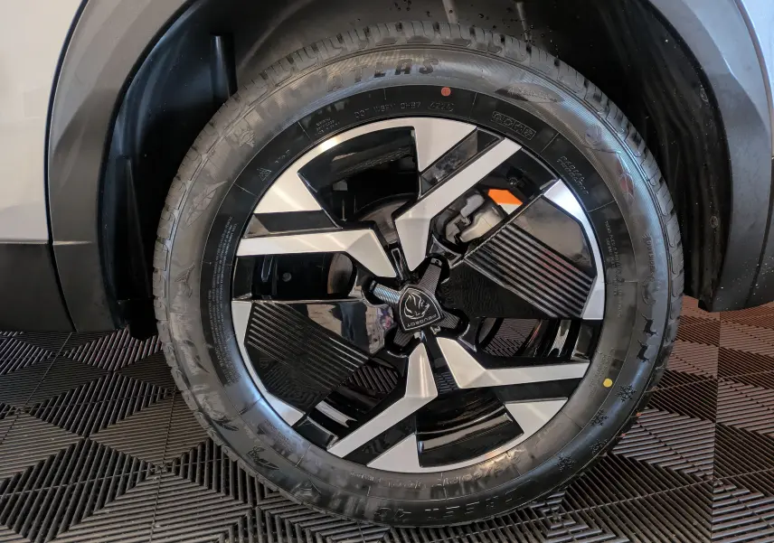 Gros plan sur la roue avant droite du Peugeot 2008 Hybrid 145 e-DCS6 GT avec jante bi-ton noire et argent.