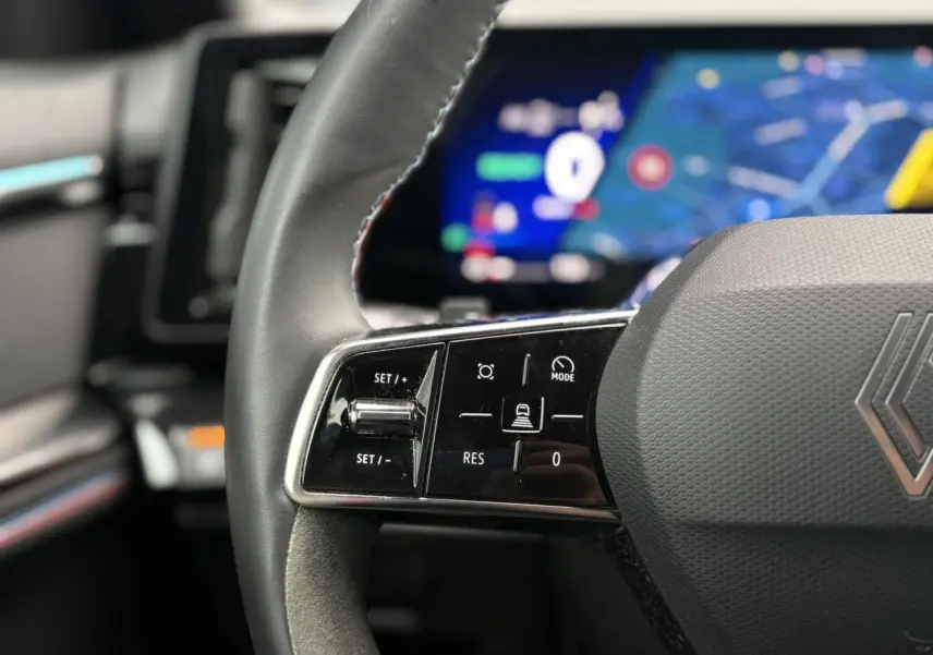 Gros plan sur le volant à droite du Renault Rafale Bleu Sommet, avec commandes intégrées et tableau de bord numérique flou en arrière-plan.