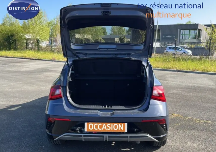 Vue arrière d'une Hyundai i20 gris Aurora Metal 2025 avec coffre ouvert sur un parking extérieur.