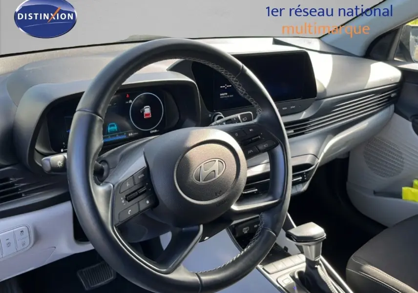 Vue intérieure centrée sur le volant cuir et le tableau de bord clair de la Hyundai i20 2025 gris Aurora Metal.