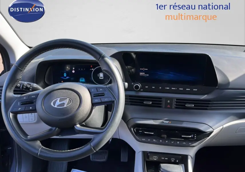 Vue intérieure du tableau de bord et volant de la Hyundai i20 2025 gris Aurora Metal avec écran tactile et commandes au volant.