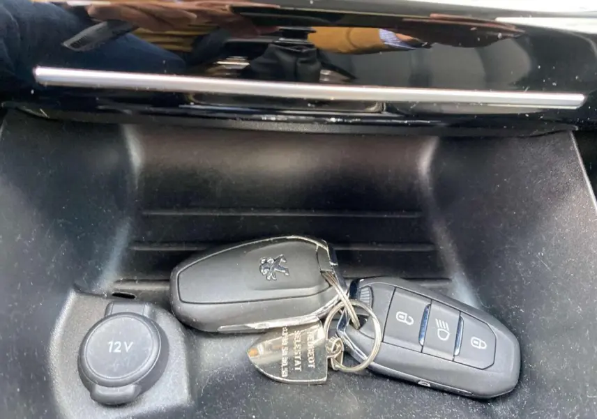 Gros plan sur les clés Peugeot posées dans la console centrale noire d'une 208 Essence 2021, avec prise 12V visible.