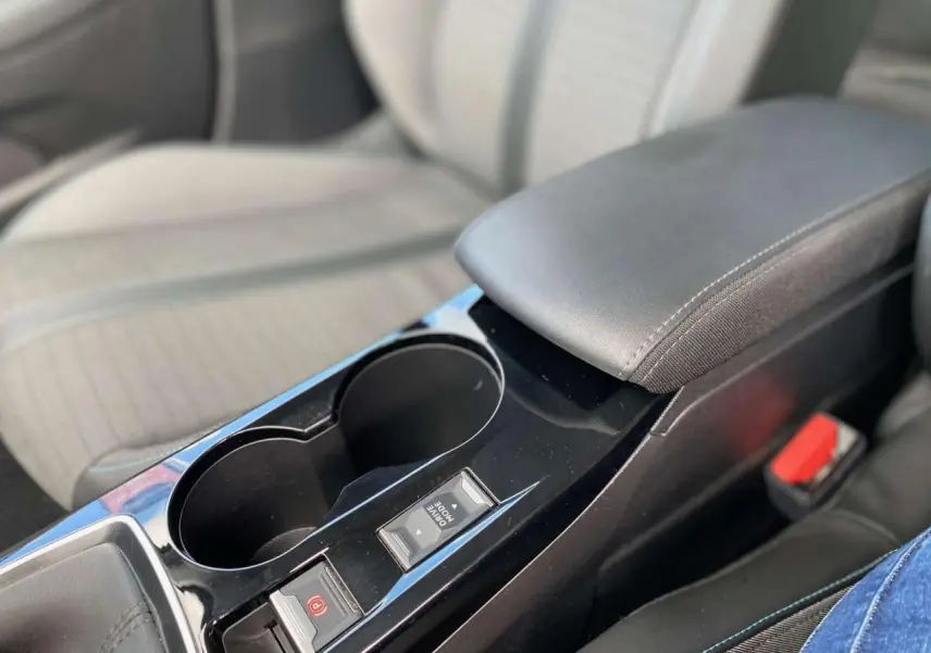 Gros plan sur la console centrale noire de la Peugeot 208 Allure 2021 avec accoudoir et boutons de frein à main électrique.