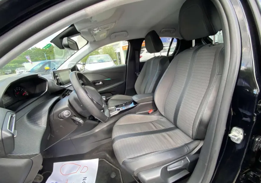 Vue intérieure côté conducteur de la Peugeot 208 noire, mettant en valeur les sièges gris clair et le tableau de bord moderne.