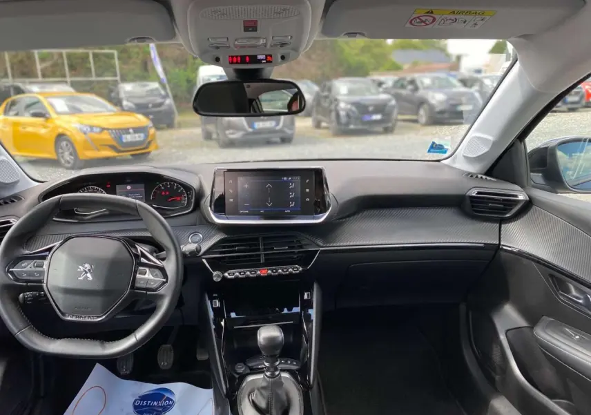 Vue intérieure avant de la Peugeot 208 noire 2021, tableau de bord moderne avec écran tactile et volant compact.