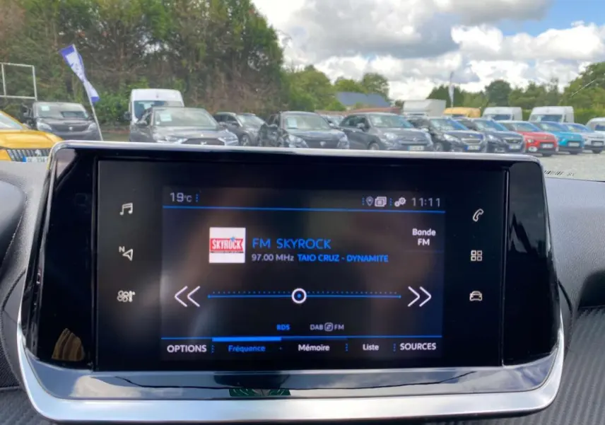 Écran tactile central de la Peugeot 208 noire de 2021 affichant la radio FM Skyrock en intérieur véhicule.