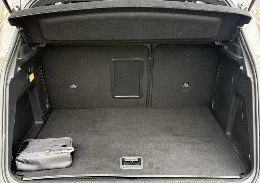 Coffre ouvert vu de l'arrière, intérieur noir avec tapis et sac de rangement, Peugeot 3008 gris Artense visible partiellement.
