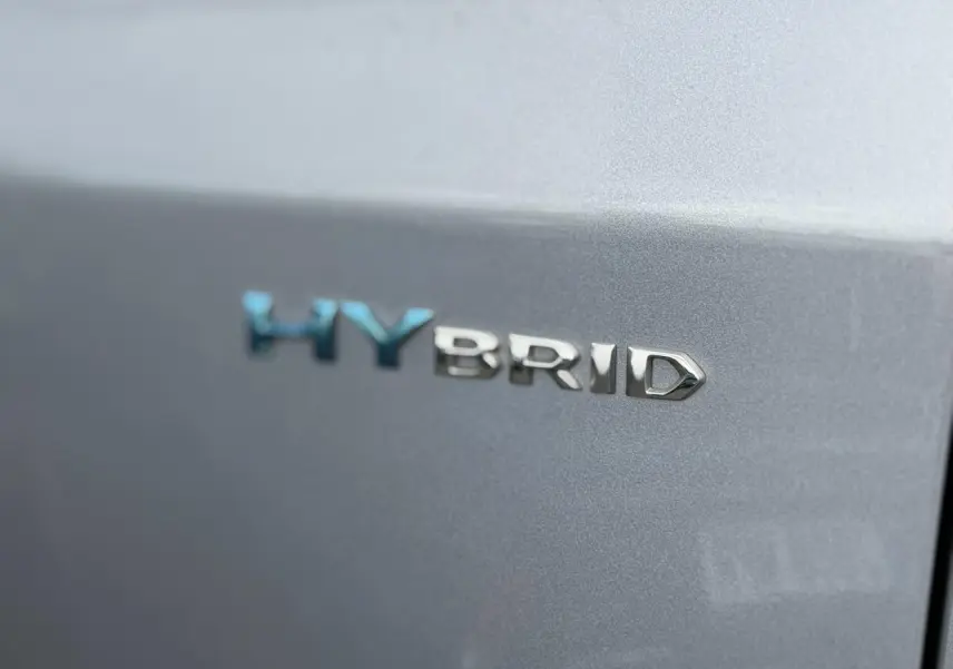 Gros plan sur le badge HYBRID bleu et chrome sur la porte arrière grise Artense d'un Peugeot 3008.
