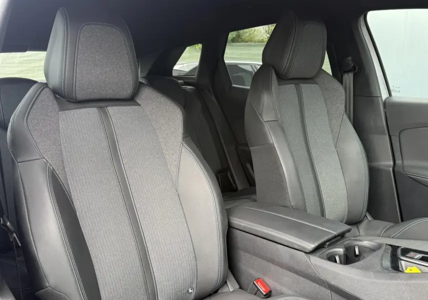 Vue intérieure rapprochée des sièges avant en tissu et cuir gris du Peugeot 3008 Plug-in Hybrid 2024 avec accoudoir central.