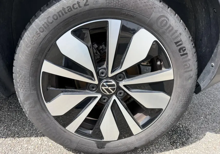 Gros plan sur la jante alliage bicolore noire et argentée d’un Volkswagen T-Roc gris, avec logo VW au centre.