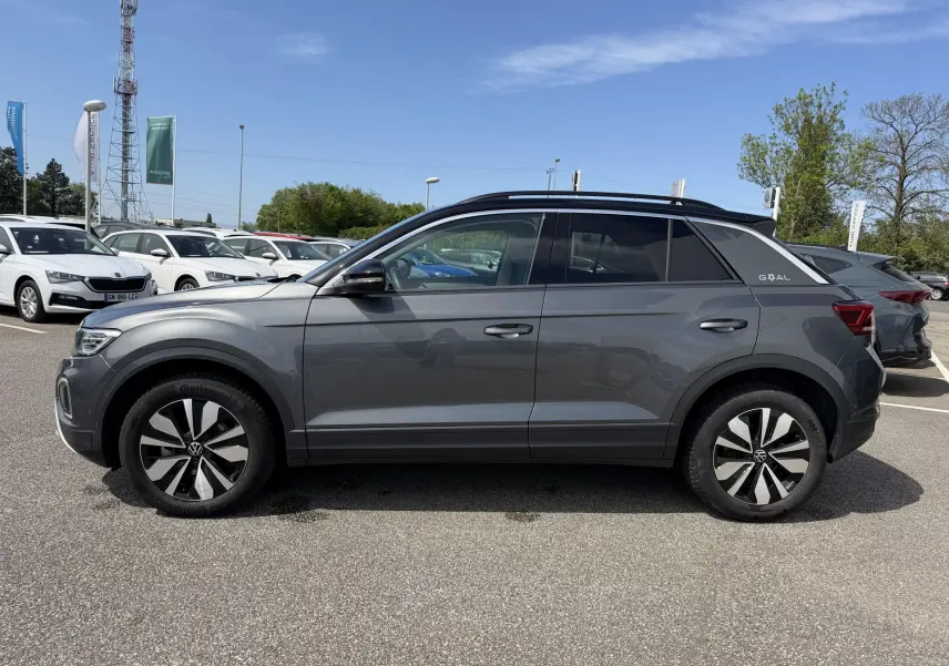 Profil droit d'un Volkswagen T-Roc gris 2025 avec barres de toit noires et jantes distinctives en alliage.