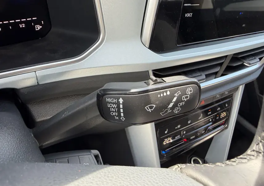 Gros plan sur le commodo d’essuie-glace du Volkswagen T-Roc gris, avec tableau de bord et commandes climatisation visibles.