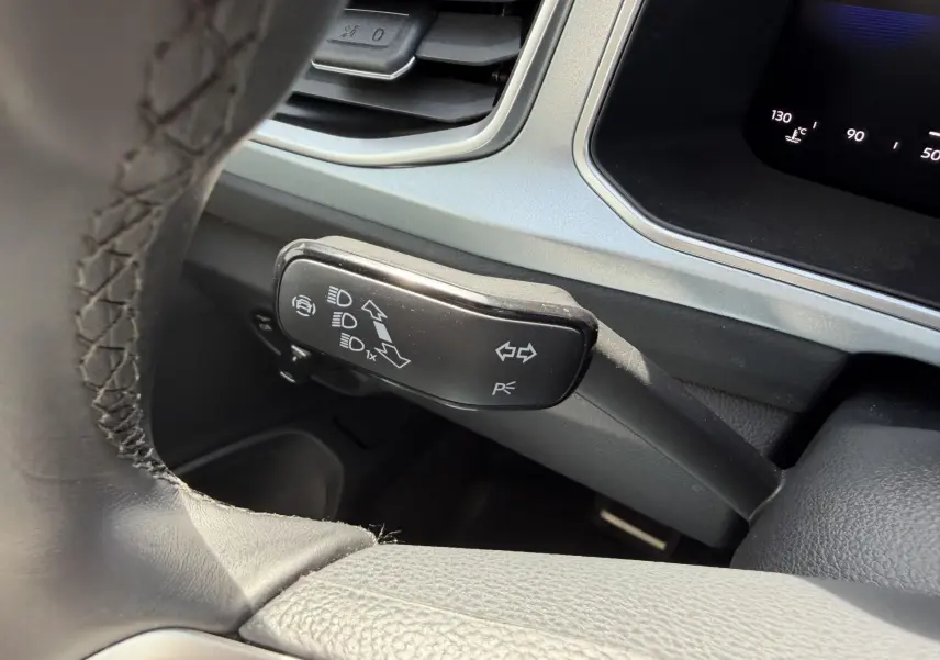 Gros plan sur la commande de clignotants et feux du Volkswagen T-Roc 2025, intérieur gris avec volant cuir noir.