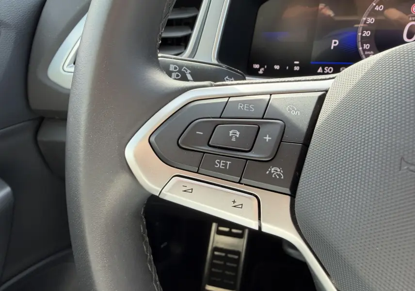 Gros plan sur le volant multifonction gris du Volkswagen T-Roc 2025, avec commandes de régulateur de vitesse et assistance au maintien de voie.