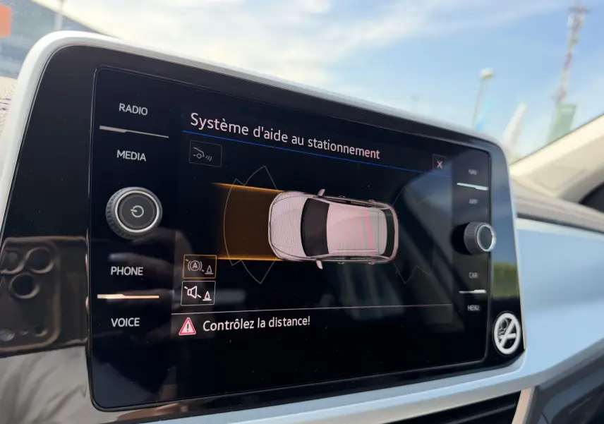 Écran tactile intérieur du Volkswagen T-Roc gris montrant le système d'aide au stationnement en fonctionnement.