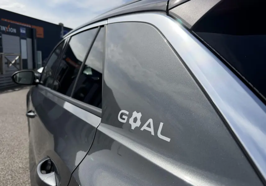 Vue côté gauche arrière d’un Volkswagen T-Roc gris métallisé avec logo GOAL sur la custode et encadrement chromé.