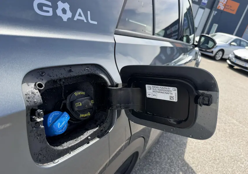Vue rapprochée du côté gauche sur la trappe de carburant ouverte d’un Volkswagen T-Roc gris avec bouchons Diesel et AdBlue visibles.