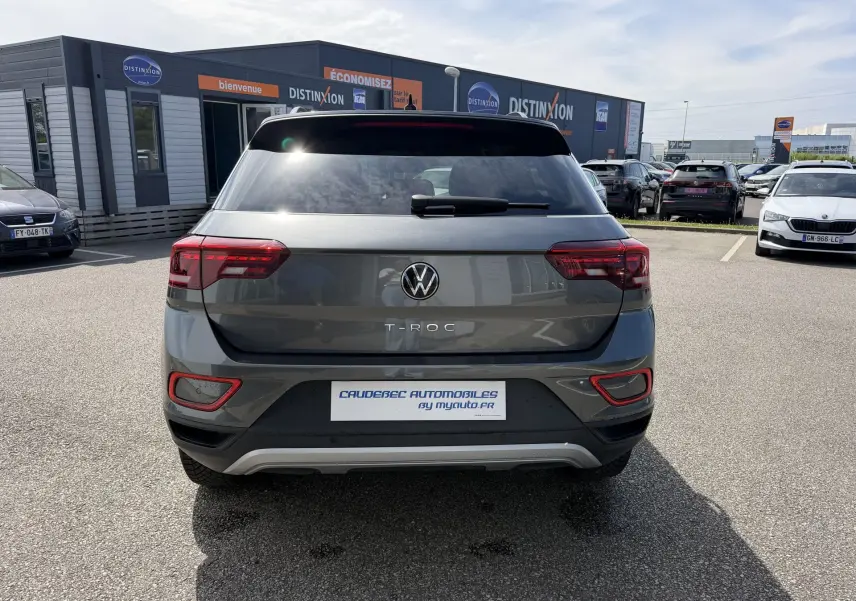 Vue arrière d'un Volkswagen T-Roc gris 2025 avec feux rouges et toit noir, stationné en extérieur sur un parking.